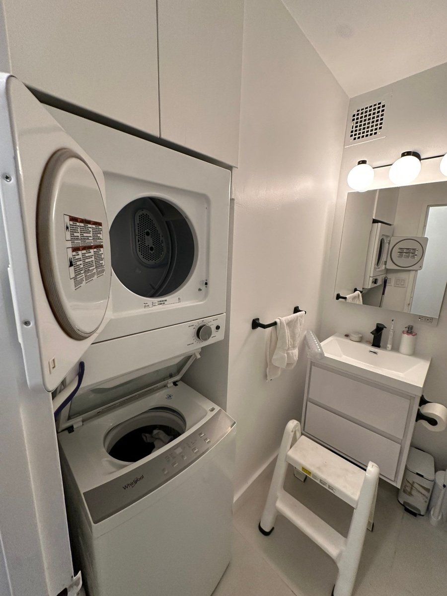 apartment renovation bathroom laundry closet with stacked whirlpool washer dryer white cabinetry and vanity in manhattan valley ny by modo renovations
