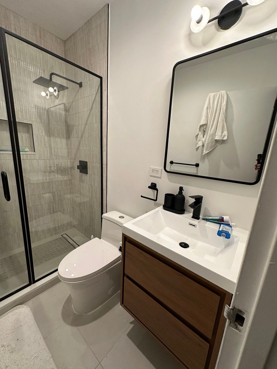 apartment renovation bathroom showing walnut floating vanity black matte faucet black framed mirror and glass shower enclosure with ribbed tile in manhattan valley ny by modo renovations