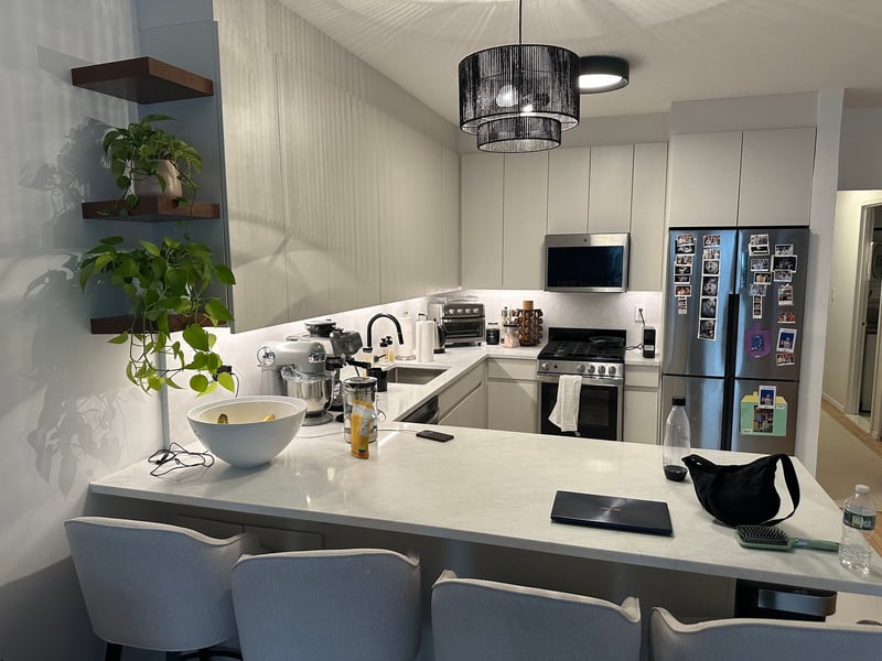 apartment renovation kitchen with marble look quartz peninsula floating walnut shelves pothos plants black pendant light and stainless appliances in manhattan valley ny by modo renovations
